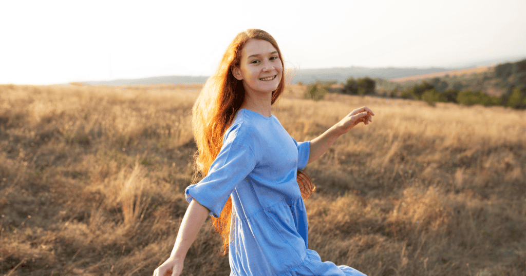 A joyful young woman in a blue dress walking freely in an open field, symbolizing stepping into clarity, independence, and light after leaving the control of a toxic family system.