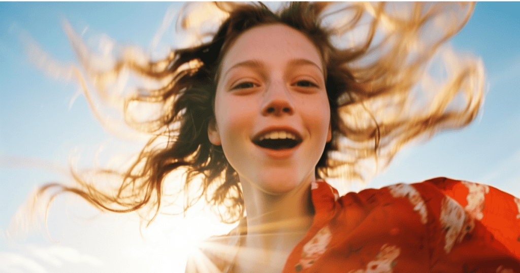 A joyful young woman with wind in her hair smiles brightly in the sunlight, symbolizing claiming the self you were never allowed to have.