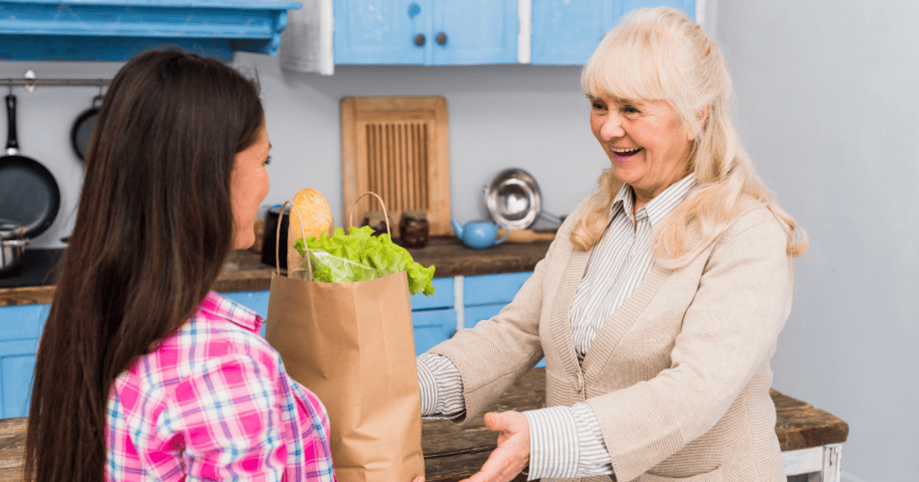 An older woman smiles while receiving groceries from a younger woman, symbolizing a narcissistic mother acting like a communal hero to her neighbor.