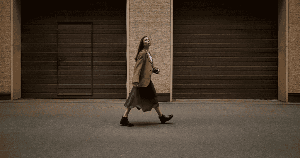 A woman strides forward with confidence, leaving the background of closed garage doors behind her, symbolizing the shift from tiptoeing around a narcissist’s chaos to walking away with strength and untouchable freedom.