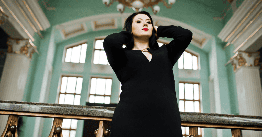 A confident woman in a black dress poses in an ornate hall, symbolizing the outward charm of grandiose narcissism that hides underlying cracks.
