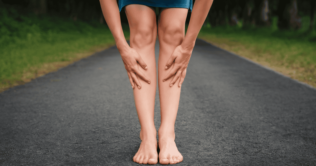 A woman stands barefoot on a road, holding her lower legs as her feet begin to go numb due to the narcissist's presence.