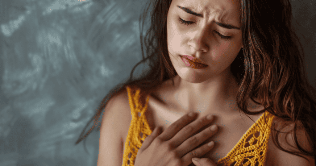 A distressed woman holds her chest with her eyes closed, feeling her heart race because of the narcissist's presence.