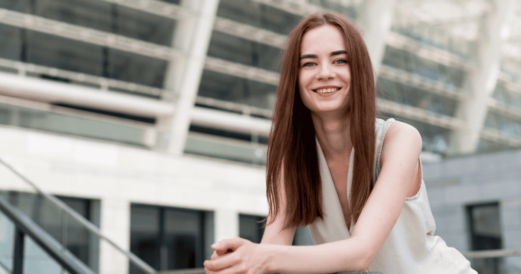 A confident young woman smiles while leaning on a railing outdoors, symbolizing how healthy narcissism differs from the toxic kind.