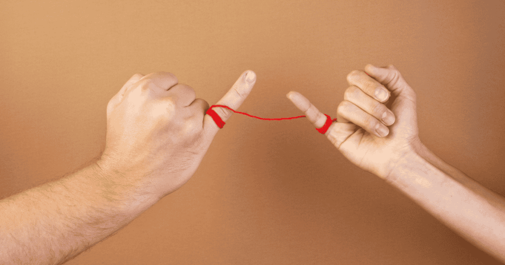 Two hands are shown with their pinky fingers tied together by a red string, symbolizing how narcissistic abuse creates unhealthy bonds that distort your natural guilt reflex.