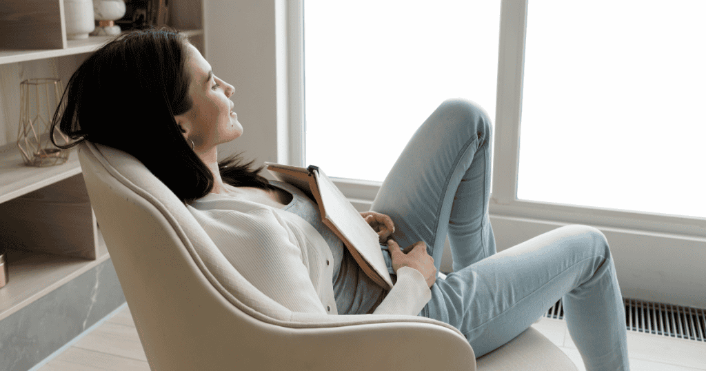 A woman sits calmly in a chair, leaning back with a notebook resting on her lap, looking peaceful and unaffected. This represents remaining composed and untouchable even when faced with narcissistic rage.