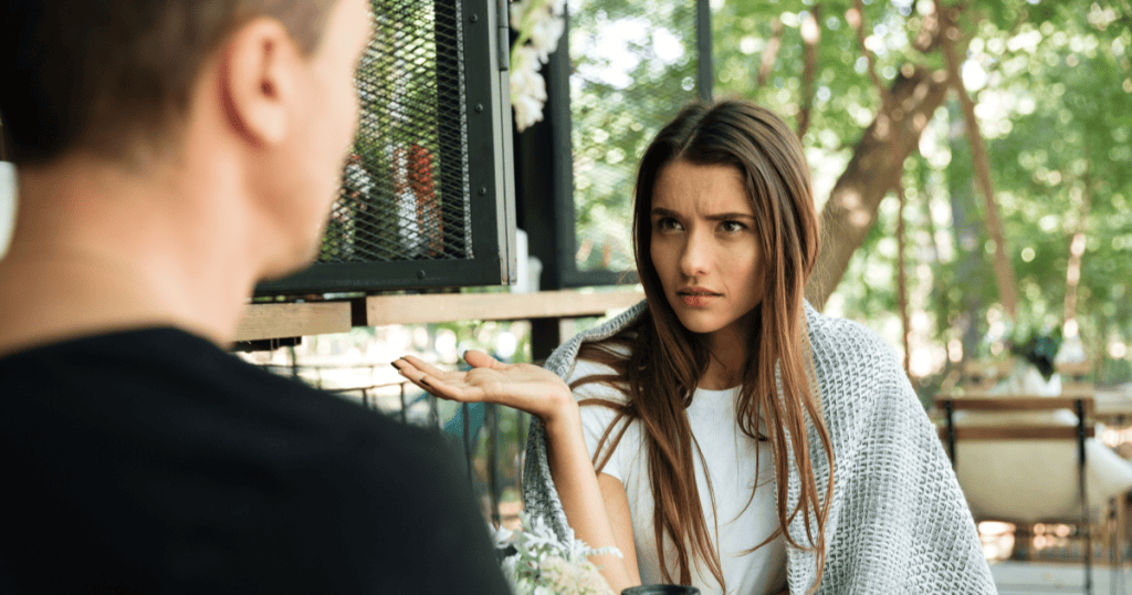 A woman raises her hand in frustration while confronting a narcissistic man during an argument.