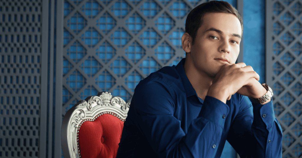 A confident man sits on an ornate red chair, symbolizing Machiavellianism and the manipulative control central to the Dark Triad.