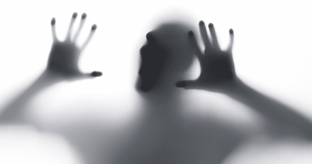 A shadowy figure presses against a screen with hands outstretched and mouth open, symbolizing the cold and disturbing nature of psychopathy.