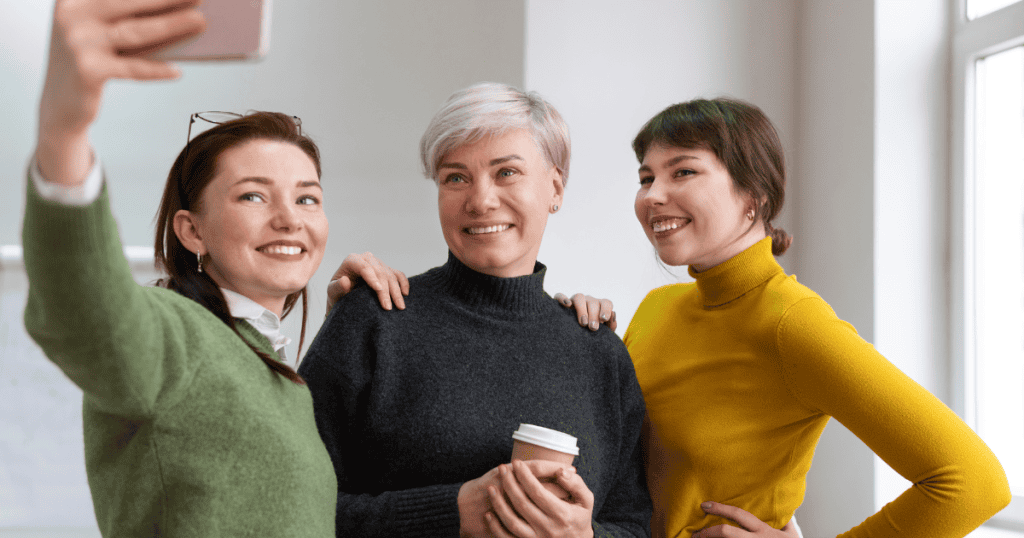 Three women smile while taking a selfie together, symbolizing the SPIN model’s third step of influence in narcissistic behavior.
