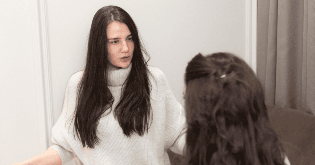 A woman in a white sweater speaks seriously to another woman indoors, representing subtle put-downs disguised as honesty.