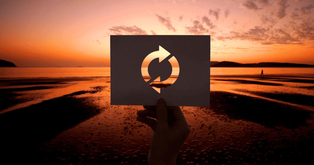 A hand holds a cutout of a circular arrow symbol against a sunset beach backdrop, representing how the cycle of narcissistic abuse resets but never truly ends.