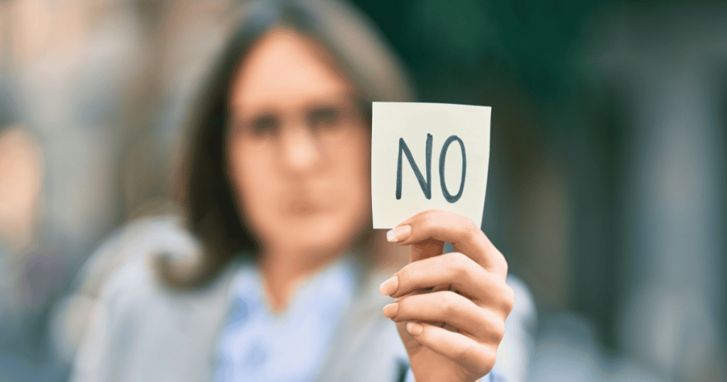 A woman holds up a note with the word “NO” written on it, symbolizing that the only way to end a narcissist’s abuse is by setting firm boundaries and refusing compliance.