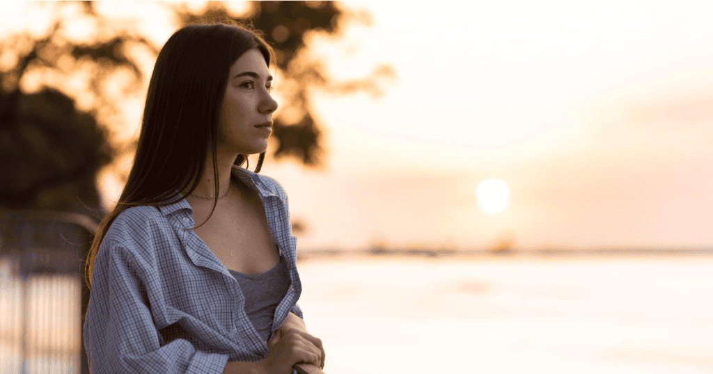A woman gazes thoughtfully at the sunset by the water, symbolizing how understanding the science behind narcissism can set survivors free.