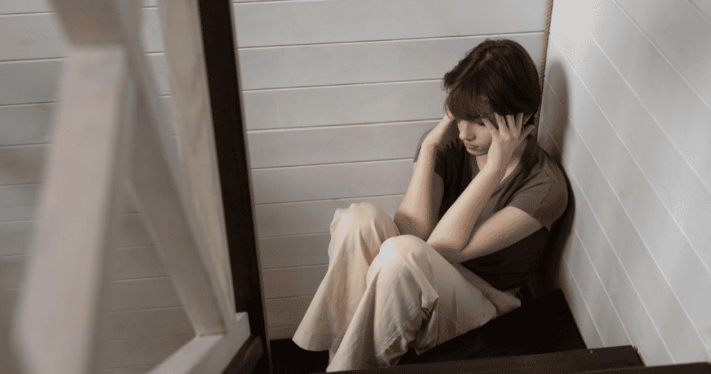 A distressed person sitting alone in a corner, holding their head, powerfully illustrating the emotional weight carried after enduring abuse.