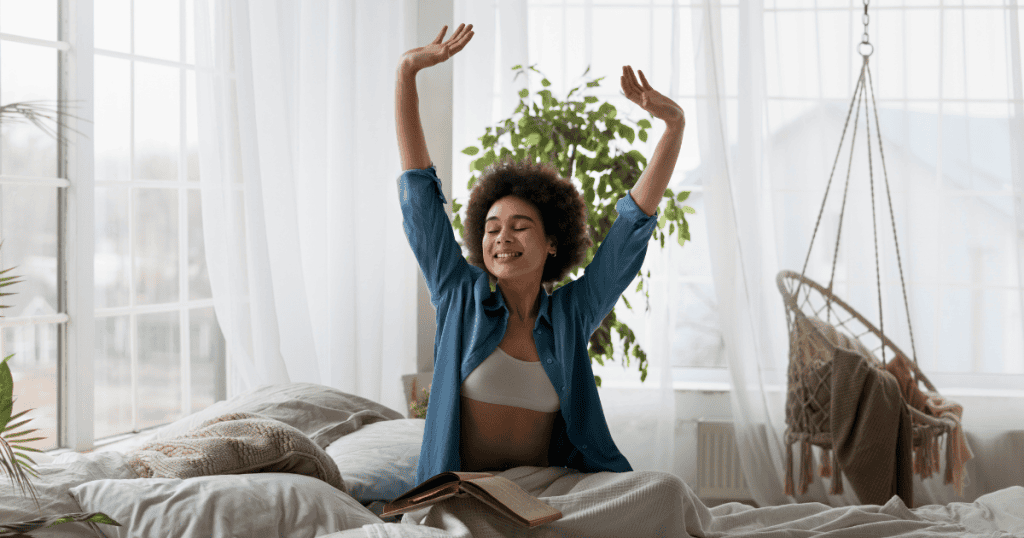 A woman stretches with a smile while sitting on her bed, symbolizing how healthy narcissistic traits like confidence and self-care can support healing.