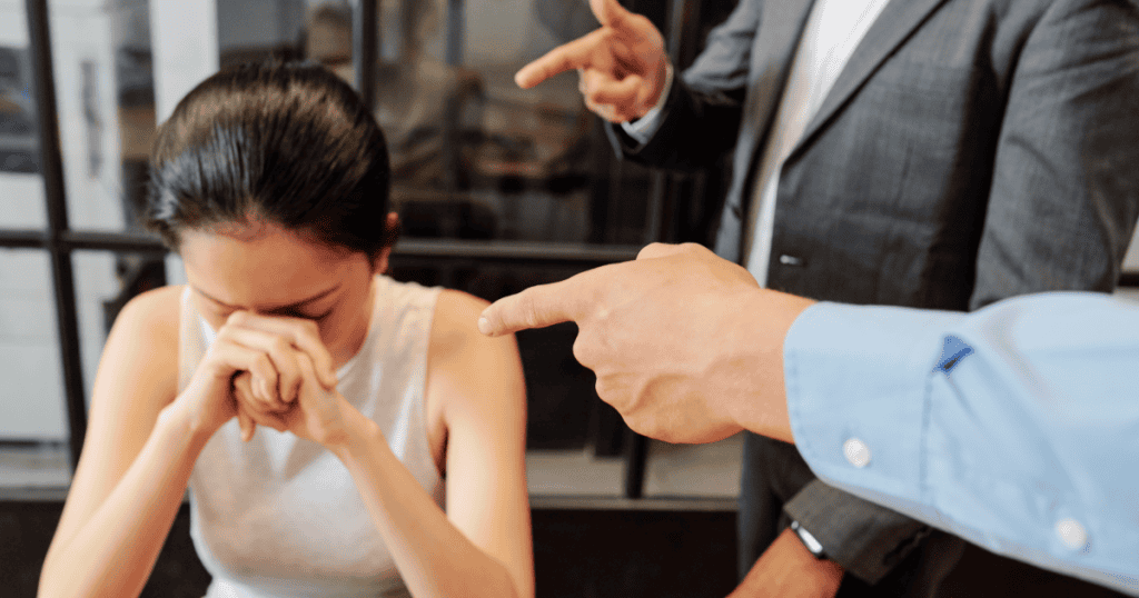 A distressed woman sits with her head down as multiple people point fingers at her, showing how narcissists project their own wrongdoings through accusations.