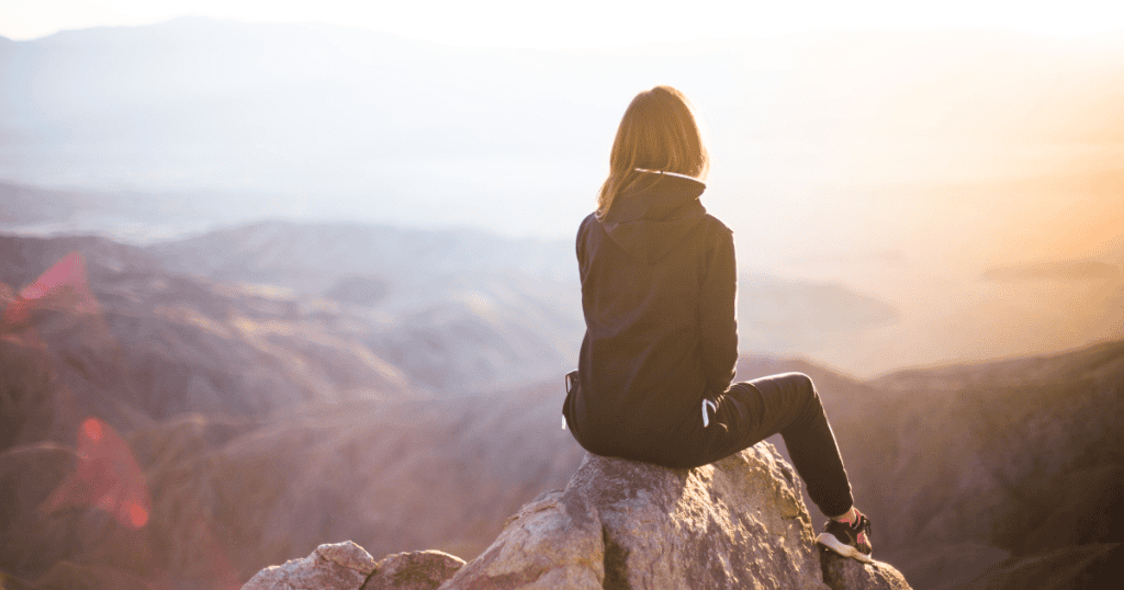 A woman sits on a mountaintop looking out over a vast landscape, symbolizing the truth that narcissists’ profiles aren’t your destiny.