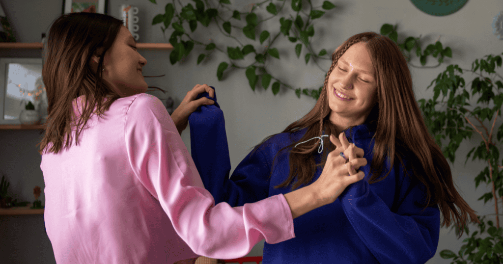 Two young women smile and dance together indoors, celebrating joy and self-care as a reminder to treat yourself like someone youโre responsible for.