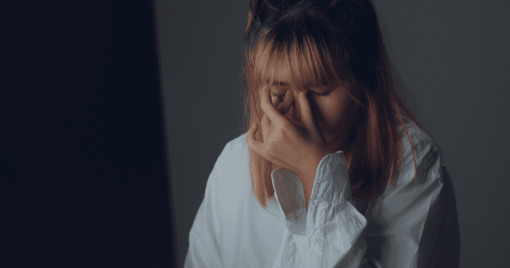 A woman in a white shirt holds her face in distress, symbolizing the fragile yet controlling nature of vulnerable narcissism.