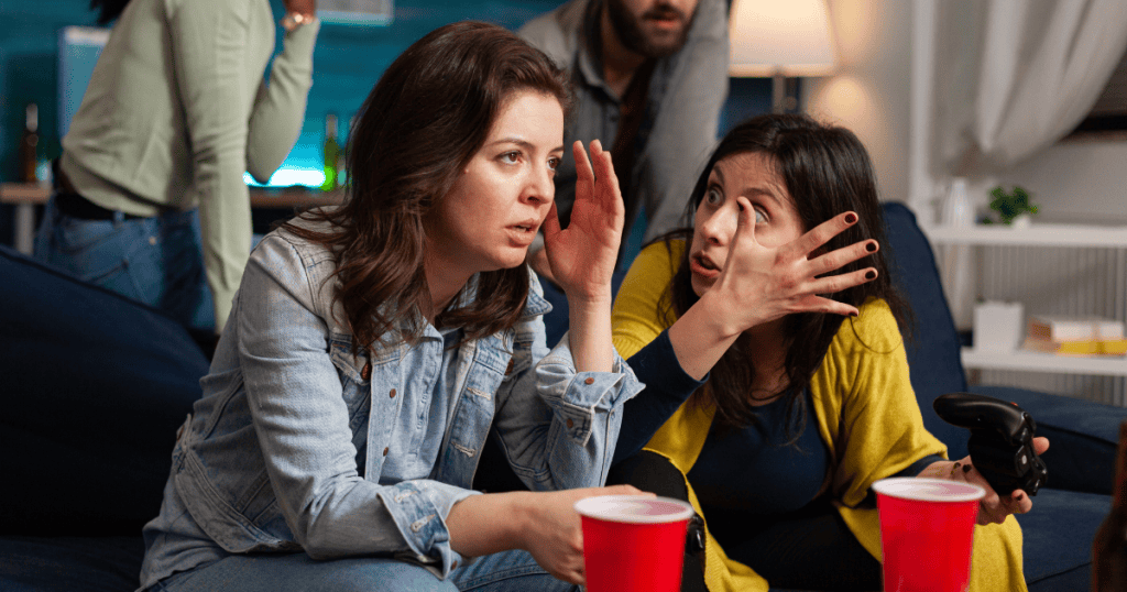 Two women in an intense conversation at a gathering, symbolizing what collective narcissism actually means, shared delusions and loyalty to protect an abuser.
