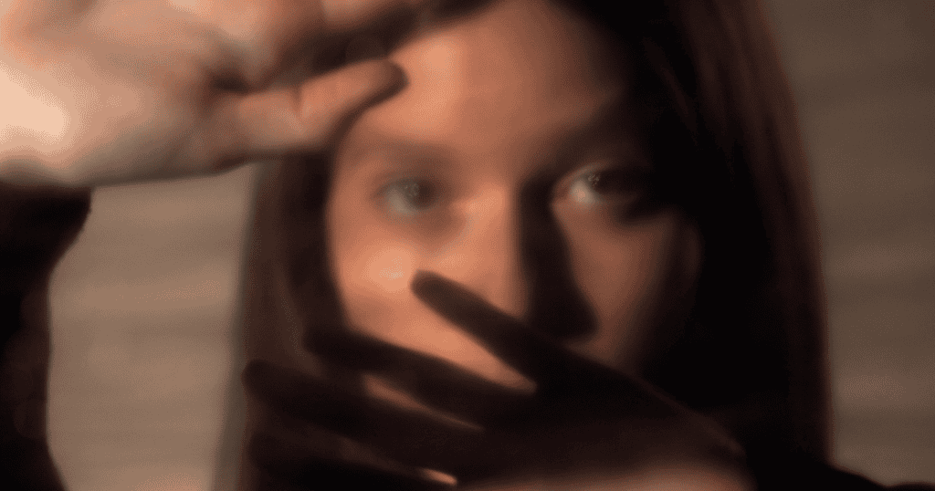 A blurred close-up of a woman with hands raised in front of her face symbolizes the moment of breaking free from the cycle of narcissistic abuse.