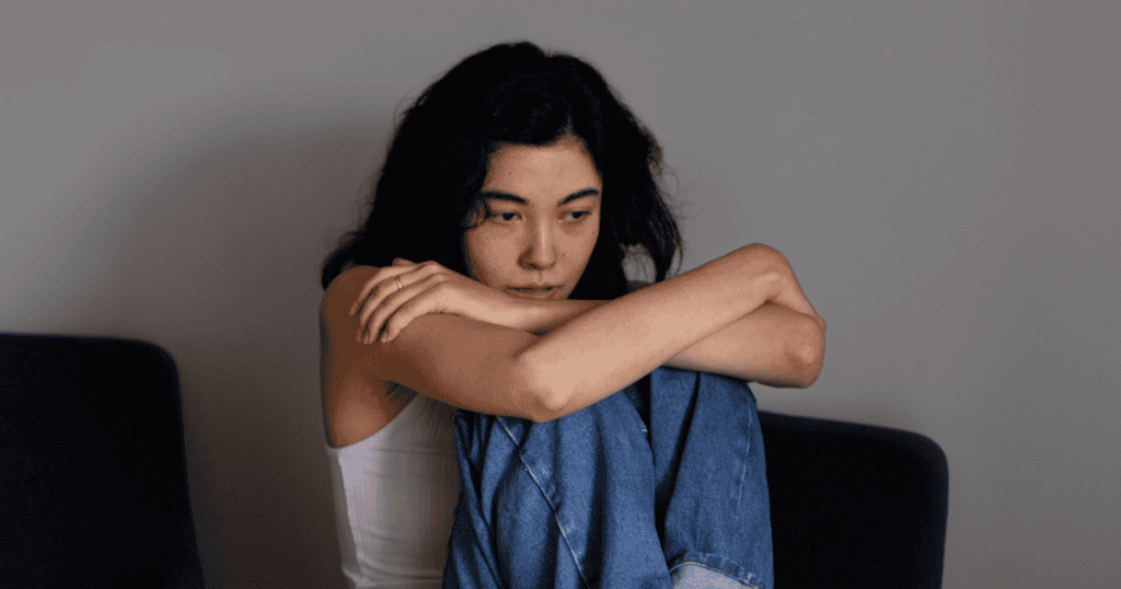 A woman sits curled up with her arms around her knees, reflecting the emotional toll survivors face when they don’t recognize a narcissist’s manipulative game.