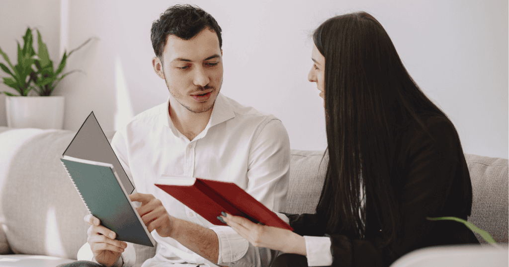 A man and woman sit together discussing notes and books, representing psychologists who studied and revealed the SPIN model’s insights into narcissistic behavior.