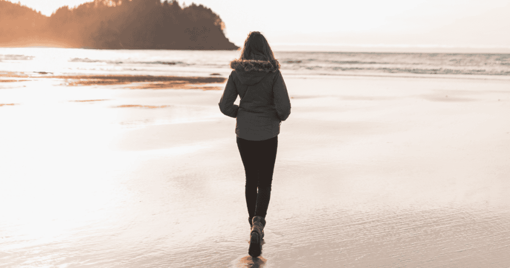 A woman in a jacket walks alone on the beach at sunset, symbolizing the strength and peace that comes from walking away when you can.