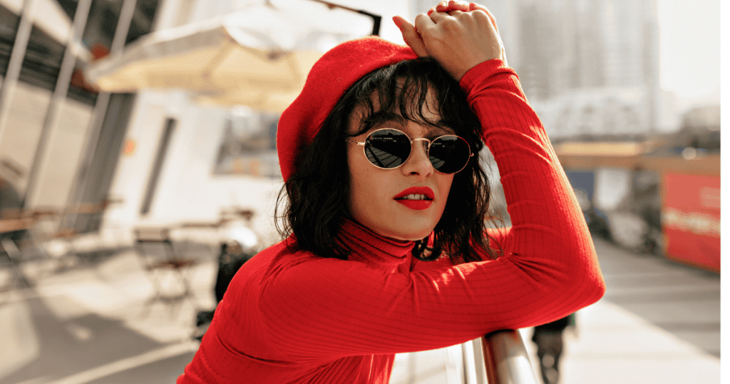 A confident woman in bold red clothes and sunglasses leans against a railing, embodying the strength that comes from no longer offering apologies that were never owed.