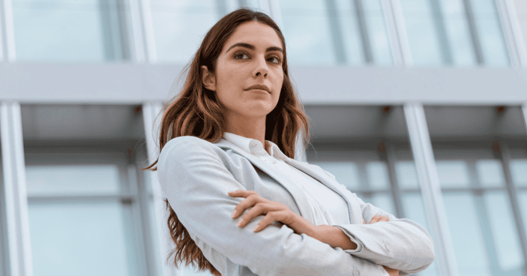 A confident woman stands with folded arms in front of a building, symbolizing the power that comes when narcissists can no longer read you easily.