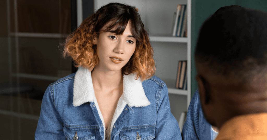 A young woman in a denim jacket listens with a weary expression during a conversation, symbolizing the draining and circular nature of talking with a narcissist.