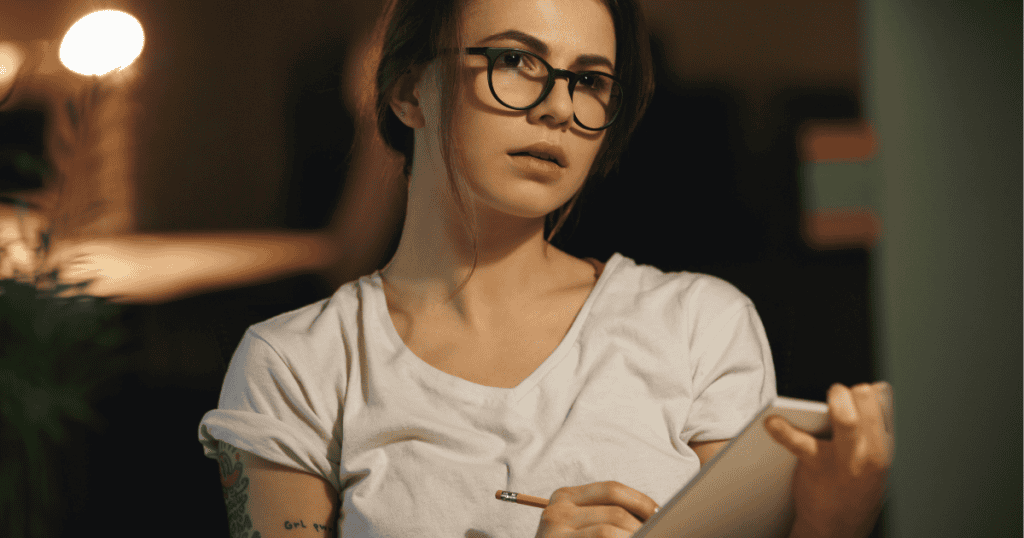 A woman wearing glasses holds a notebook and pencil while looking thoughtful, symbolizing how gaining knowledge about narcissists can change everything for survivors.