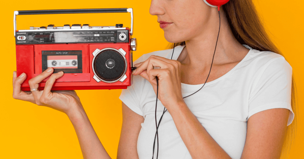 Woman in white shirt listening to music on headphones while holding a red retro cassette player against a bright yellow background; reflects the idea of putting empowering truths on repeat, just like a favorite song.