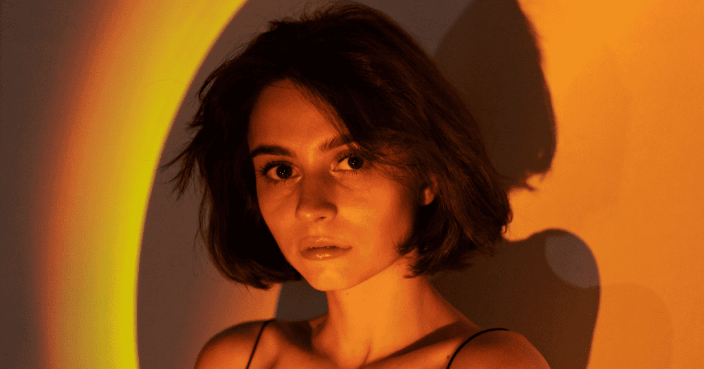 A young woman with short brown hair looks directly at the camera under warm golden lighting, illustrating the idea of why your glow threatens every narcissist.