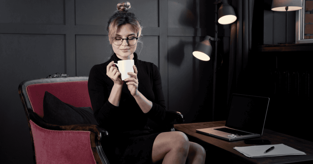 A woman sits calmly with a cup of coffee in a dimly lit office, symbolizing the quiet strength of winning without engaging in a narcissist’s manipulative game.