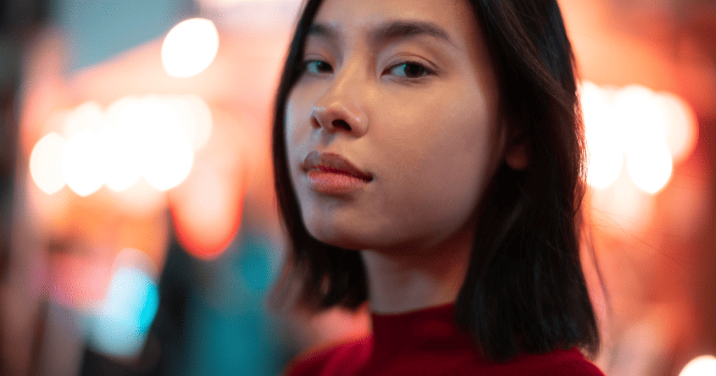A woman in a red top looks directly at the camera with a steady gaze, symbolizing how narcissists study your expressions and body language to read you.