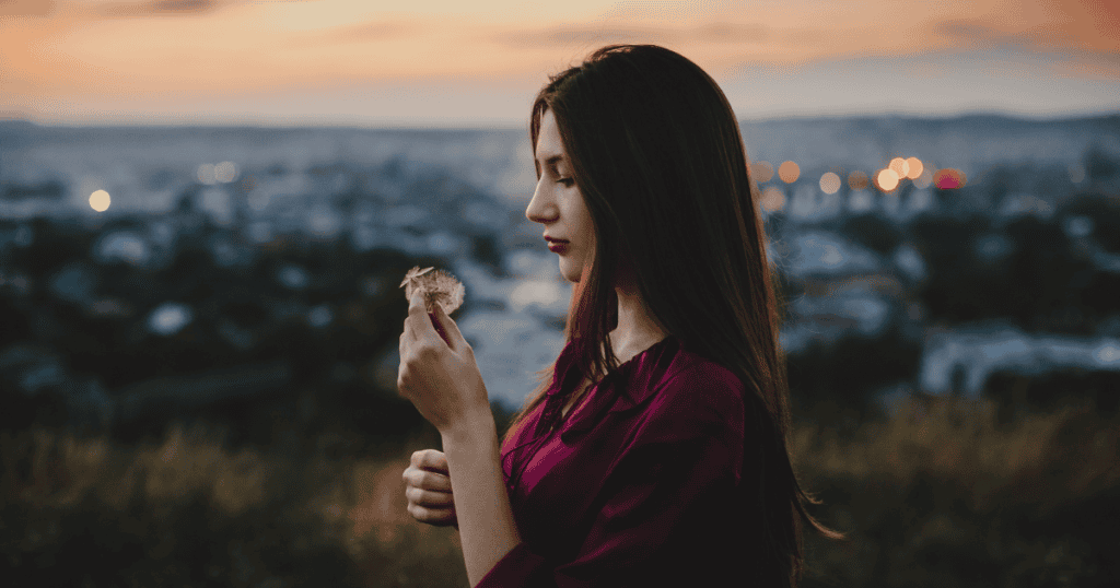 A woman stands outdoors at sunset holding a dandelion, symbolizing the quiet strength of survivors whose truth about narcissistic abuse deserves to be believed.