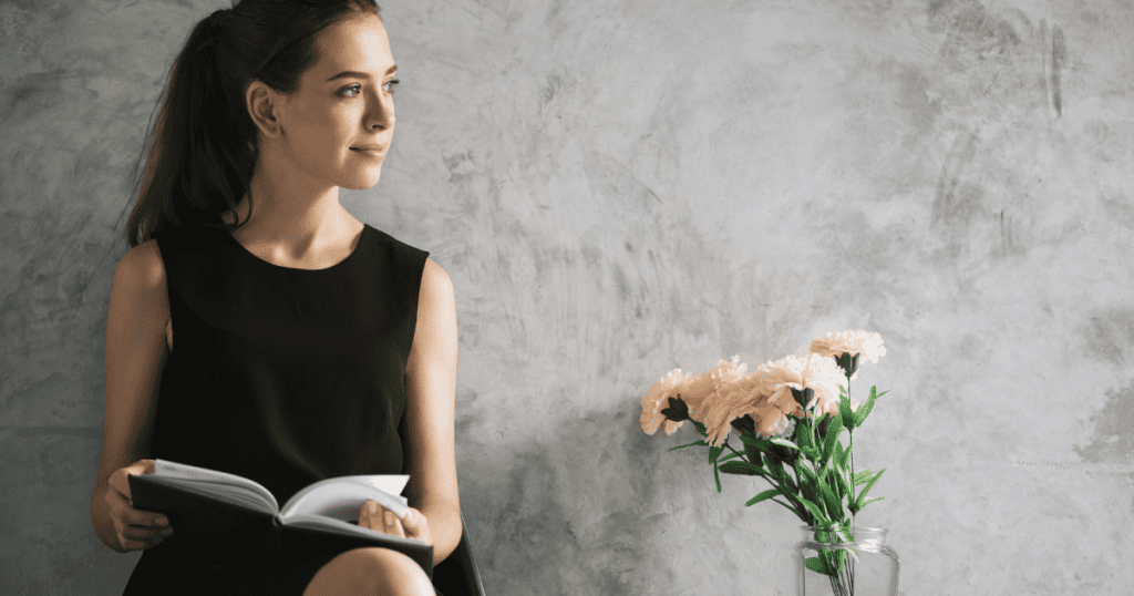 A young woman with her hair in a ponytail sits reading a book with a vase of flowers next to her; her reflective pose is essential for turning the opposition's tactics back on them.
