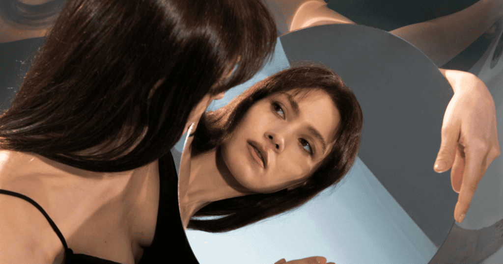 A woman looks at her reflection in a mirror with a thoughtful expression, representing the importance of mastering boundaries to stop attracting narcissists.