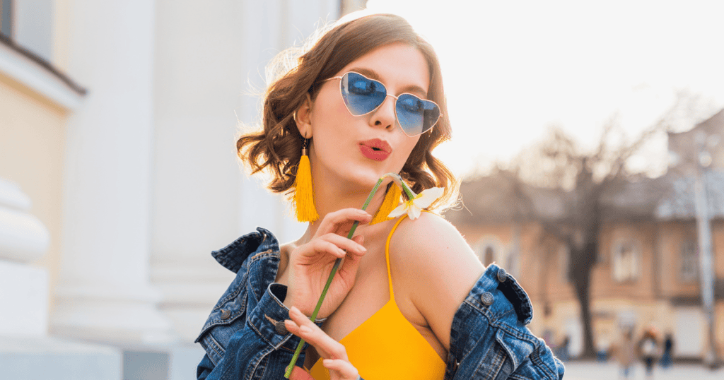 A confident woman in bright colors and heart-shaped sunglasses holds a flower, embodying self-assurance and the power to say “no” without guilt.