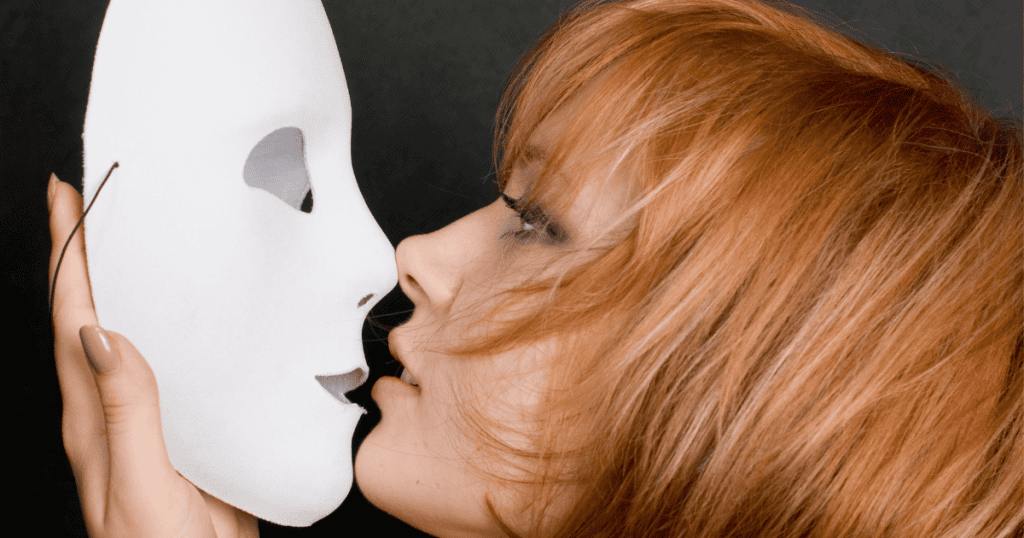 A woman with red hair holds a white mask close to her face, representing the theme of seven masks narcissists hide behind and how to rip them off.