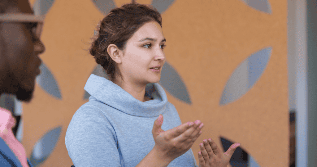 A woman speaks calmly while gesturing with open hands, representing confidence in setting boundaries and no longer apologizing for her personal growth.