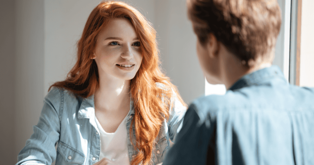 A confident woman speaks calmly to someone across the table, using a composed and intelligent tone that subtly challenges without confrontation.