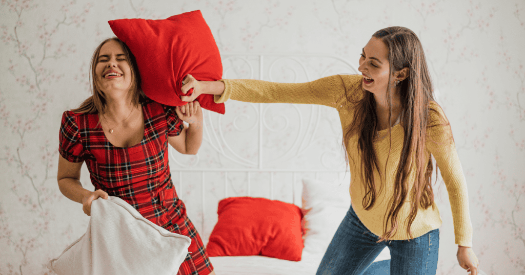 Sisters are playfully having a pillow fight on a bed, highlighting the initial, intense excitement and good feelings of a deep connection.