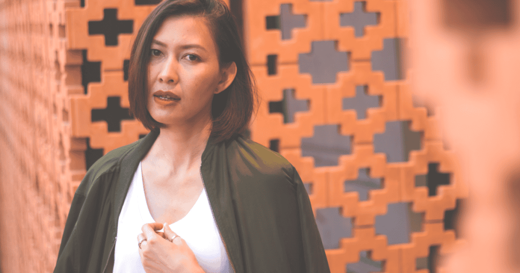 A woman stands against a patterned wall with a calm but guarded expression, symbolizing emotional detachment and the quiet strength that follows the end of a manipulative cycle.