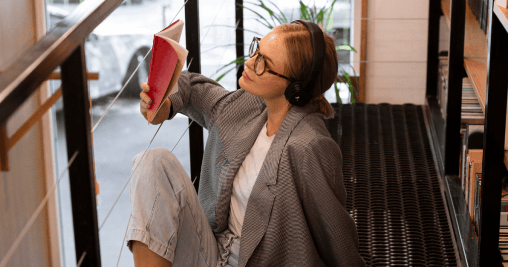 A woman wearing headphones and glasses sits on a stairway reading a book, illustrating the focused self-boundaries needed to tell a narcissist something isn’t aligned with her priorities.