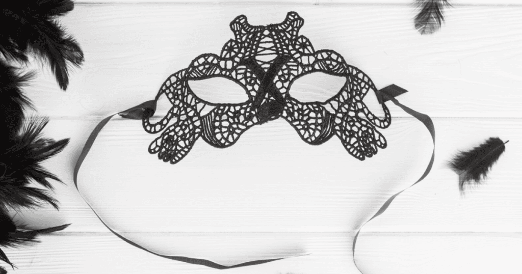 A delicate black lace mask with feathers scattered around it on a white surface, symbolizing the broken mask.