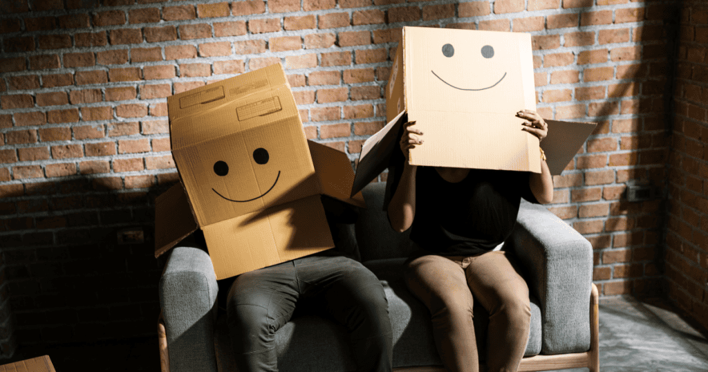 Two people sit on a couch with boxes over their heads featuring smiley faces, representing the emotional boundary.