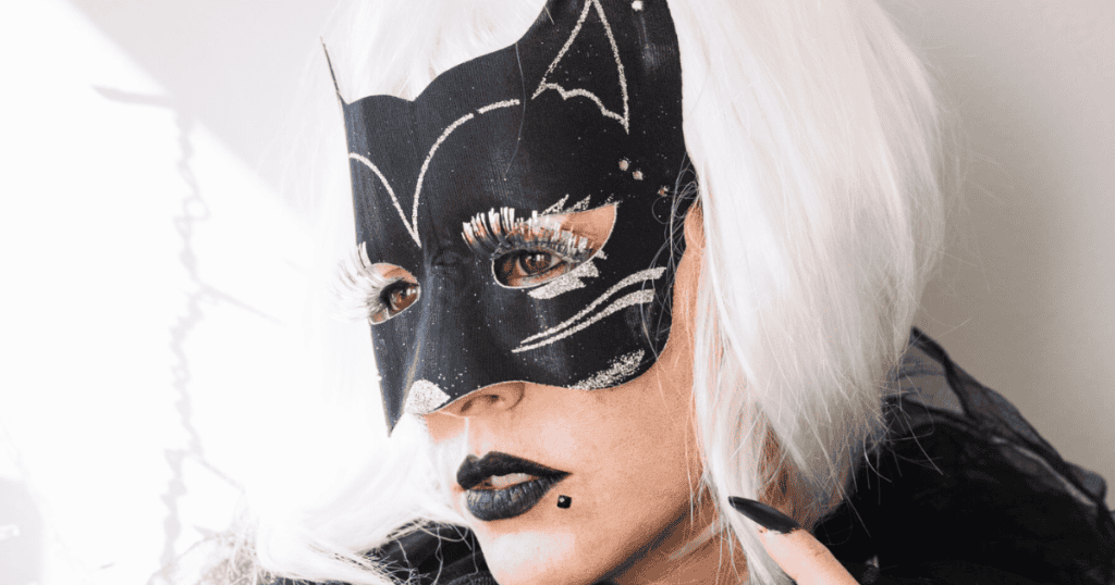 A person wearing a black cat-shaped mask with glitter details and a white wig, representing the hardworking mask.